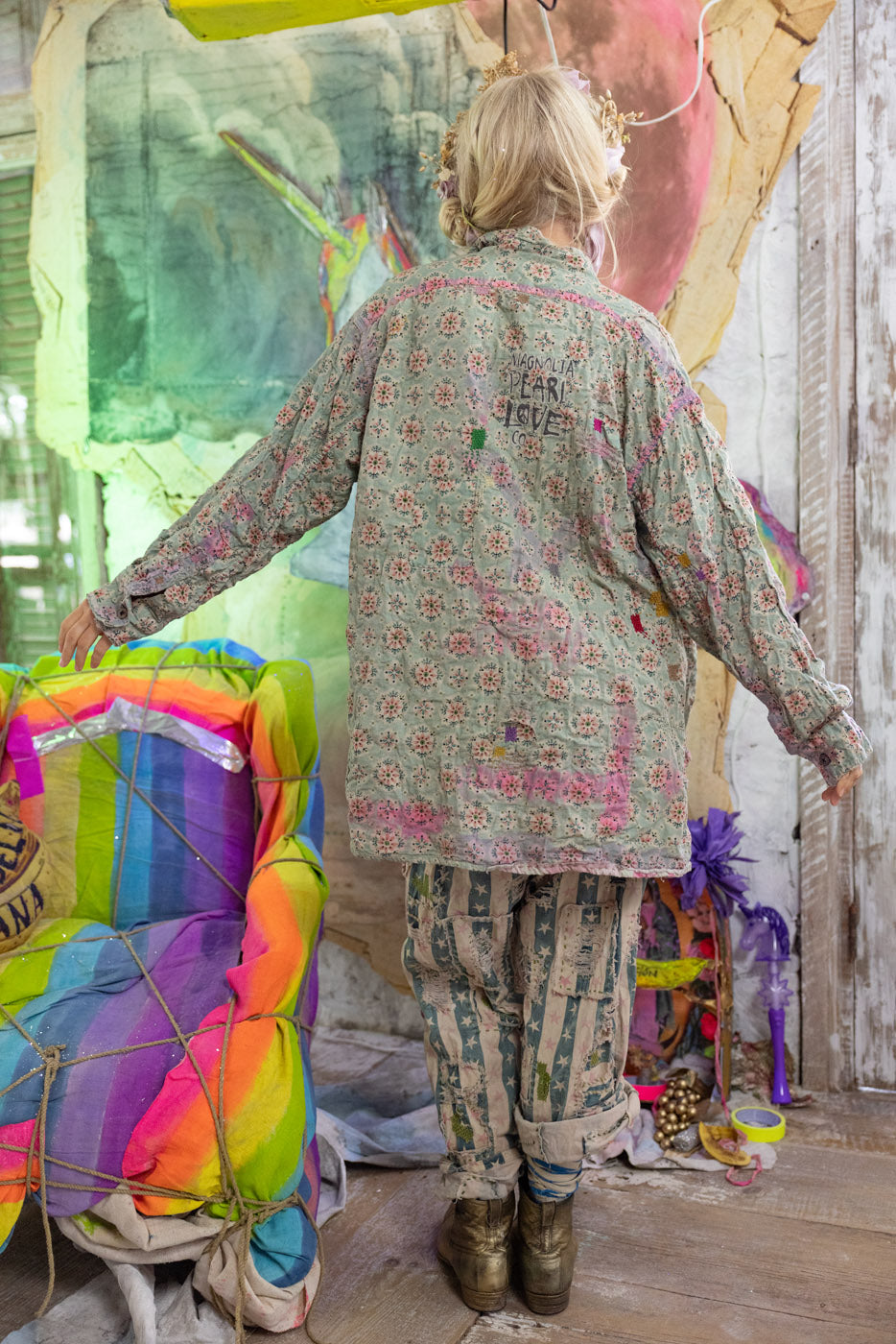 Person wearing a patterned blouse and pants in a colorful, artistic setting.