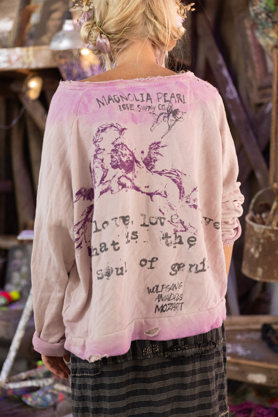 Person wearing a light pink Mozart sweatshirt with purple text and graphics, standing in a casual setting.

"Love, love, love, that is the soul of genius," quote on the back.