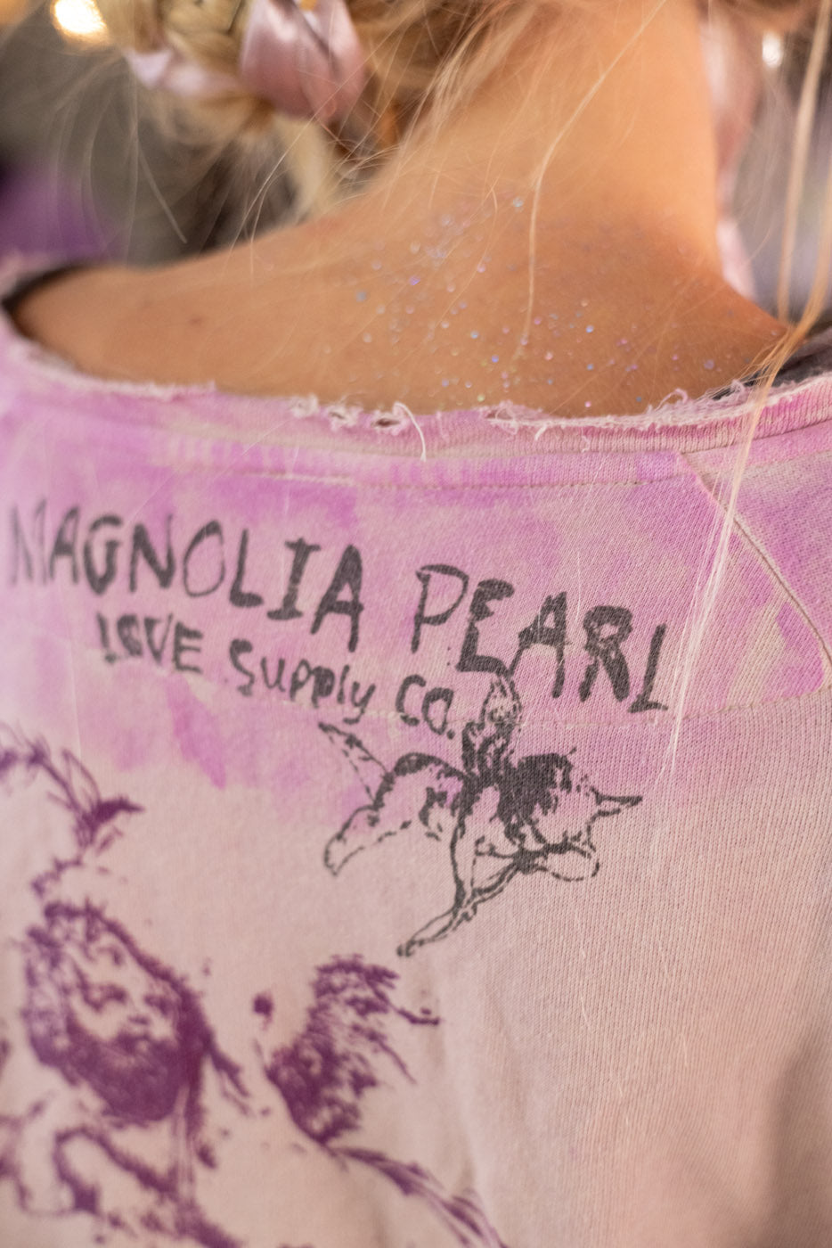 Close-up of a shirt with 'Magnolia Pearl Love Supply Co.' text and angel design.