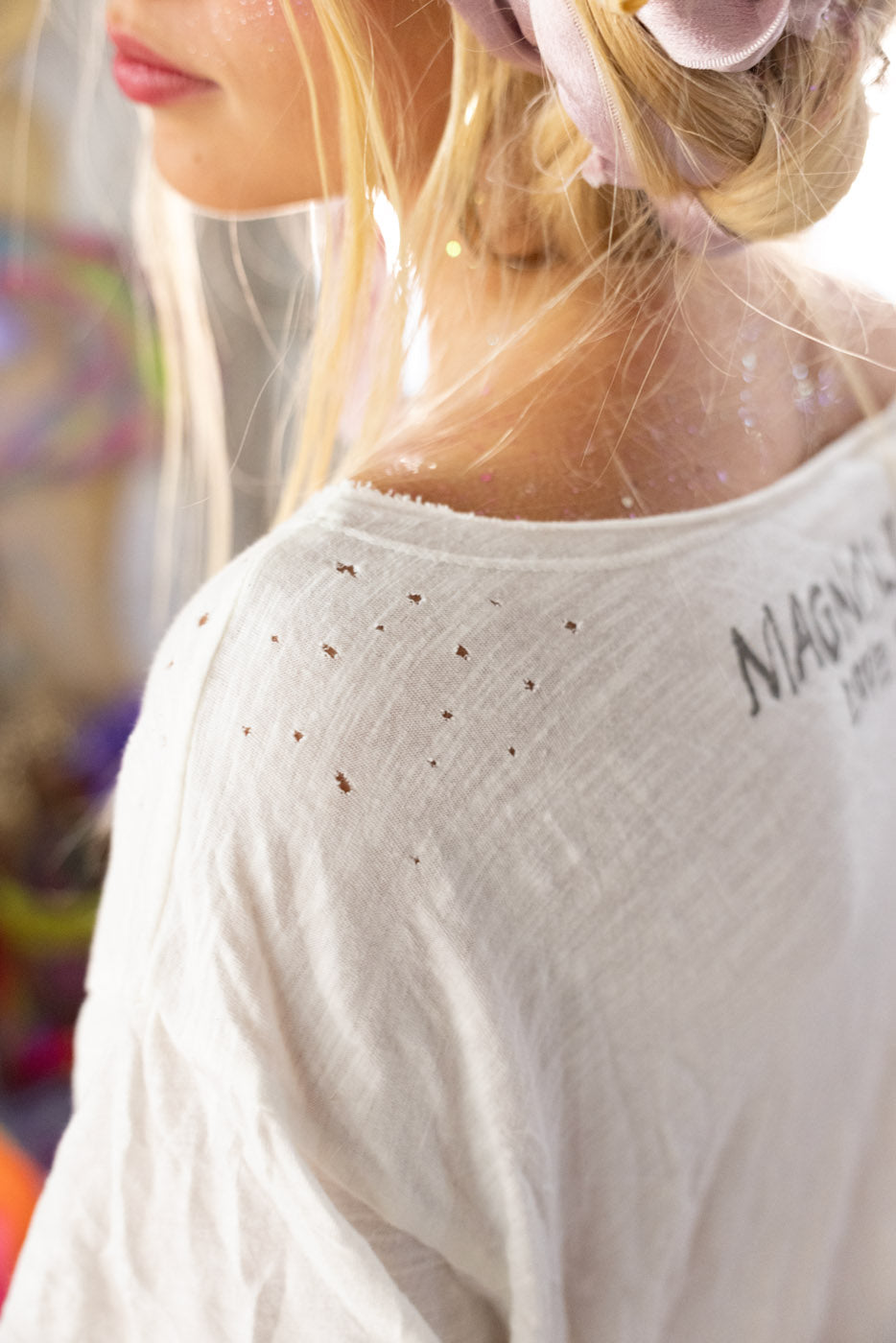 Close-up of a person wearing a white top with 'Magnolia Pearl' branding, blurred background