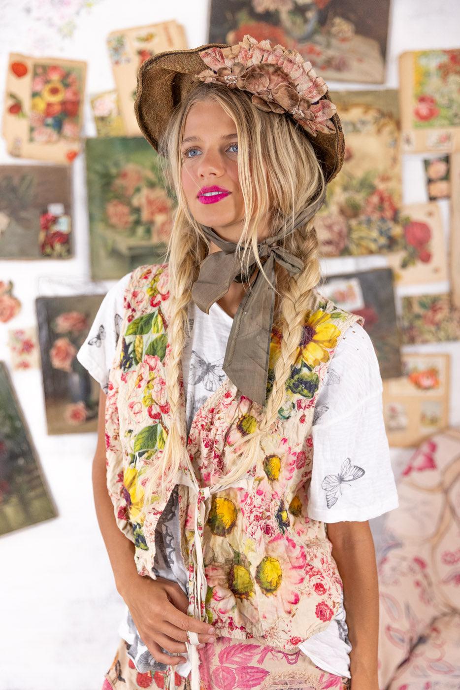 Woman in Magnolia Pearl artisan floral vest, whimsical vintage hat, boho style, colorful art backdrop