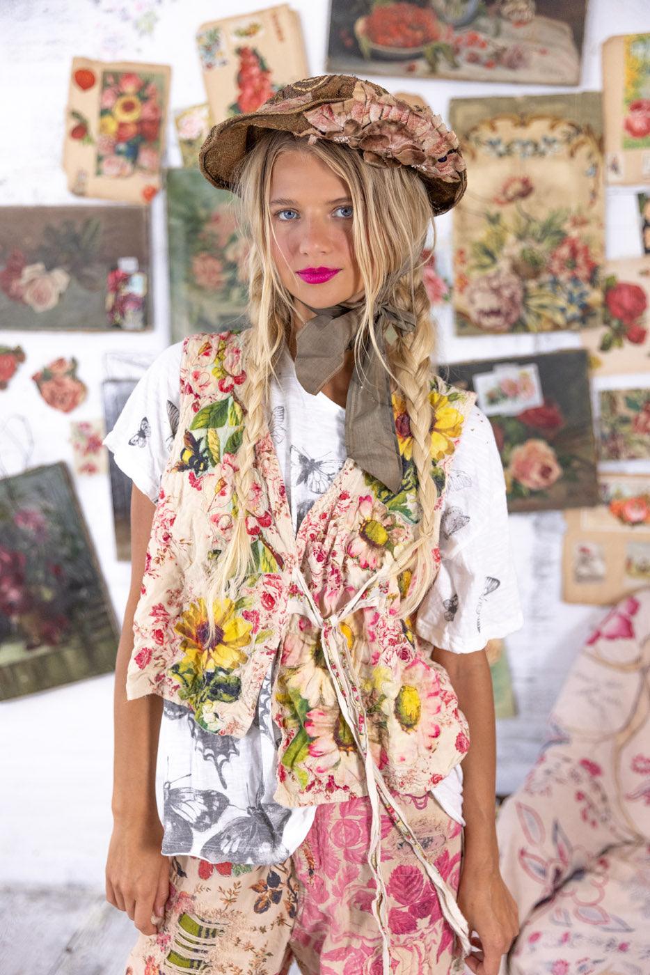 Woman in Magnolia Pearl artisan floral vest, whimsical vintage hat, boho style, colorful art backdrop
