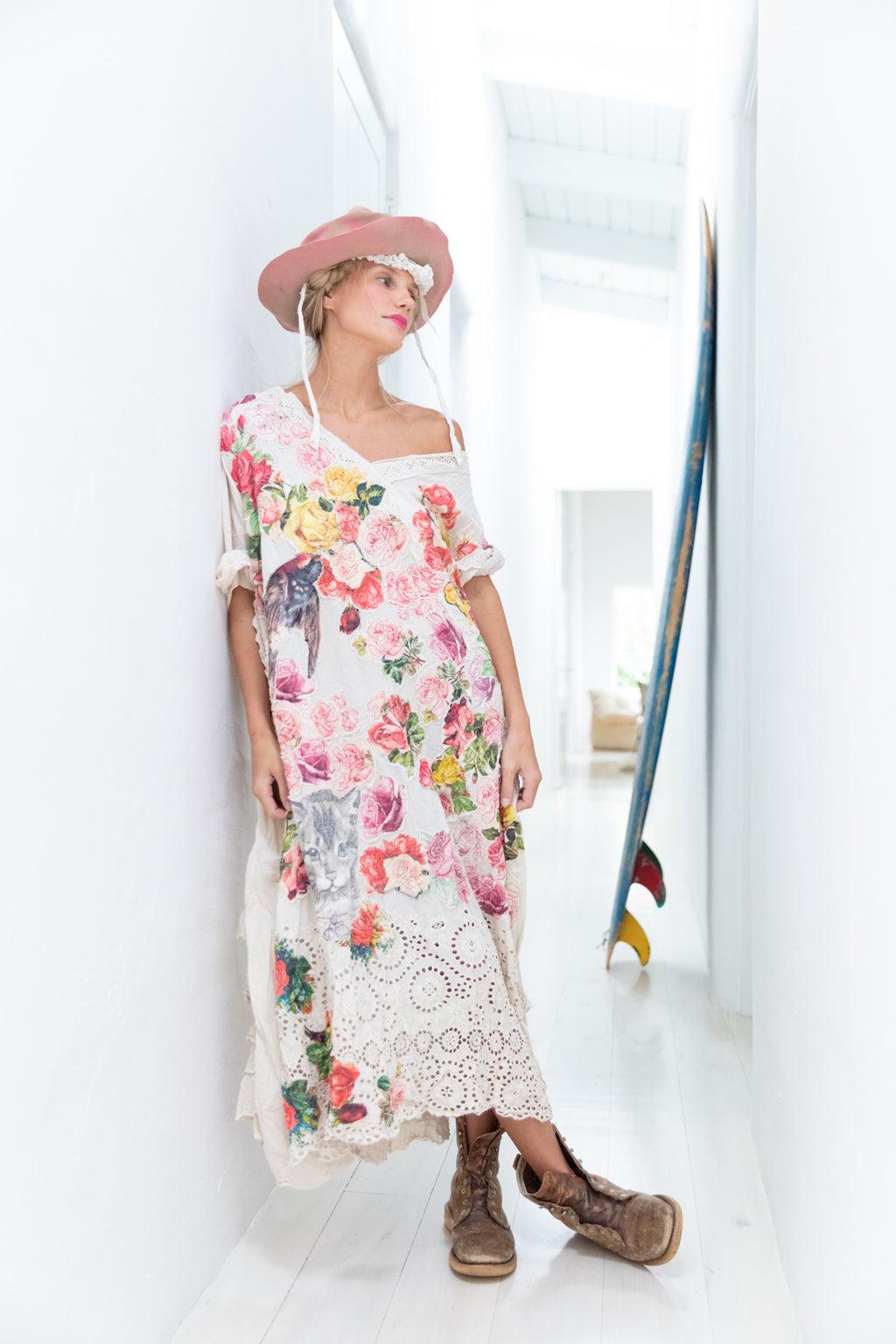 Woman in Magnolia Pearl artisan floral dress, vintage lace, pink hat, and boots, leaning in bright hallway
