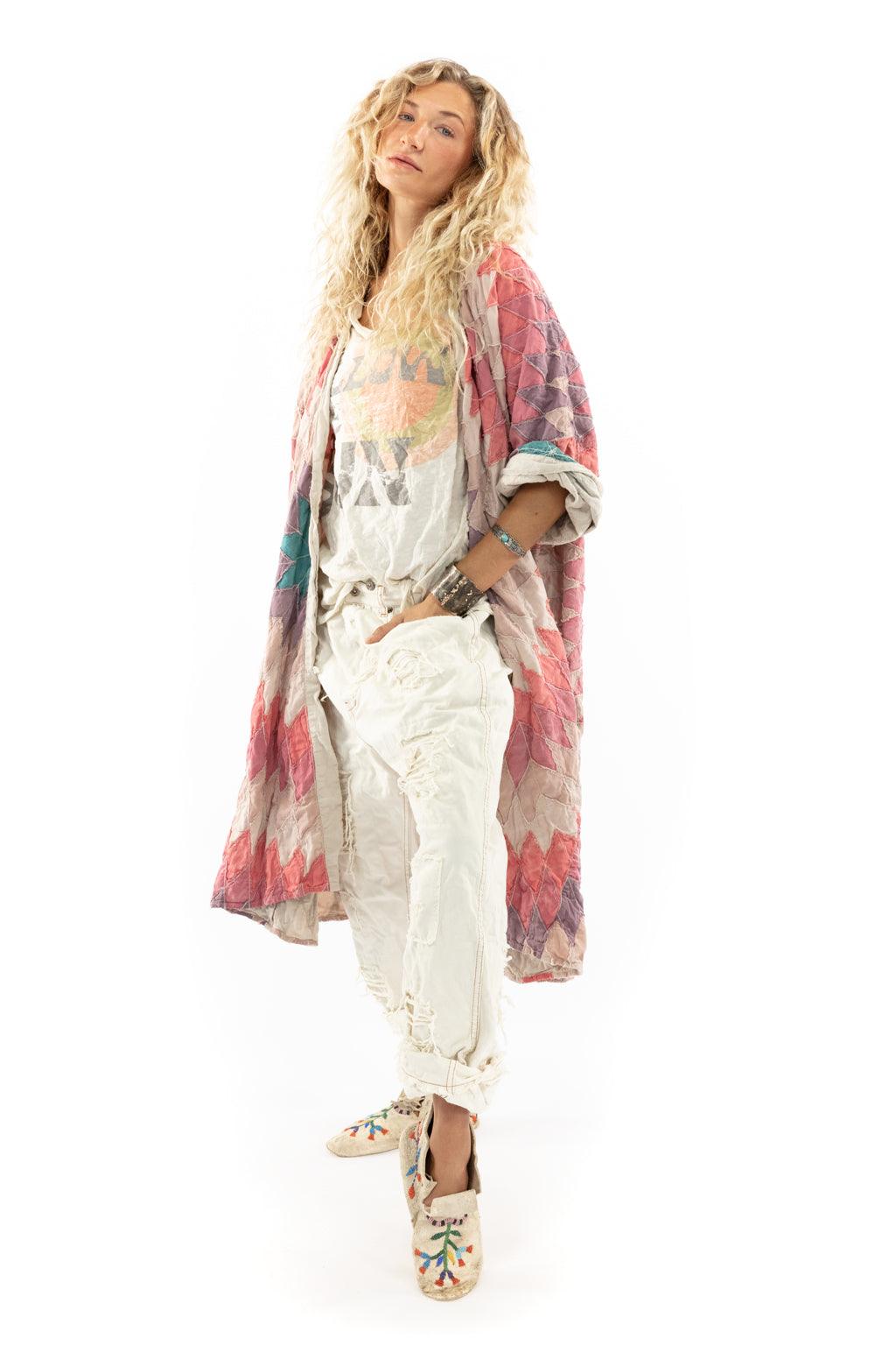 Woman models Magnolia Pearl artisan jacket with whimsical patchwork design, vintage distressed pants and boho shoes on white background.