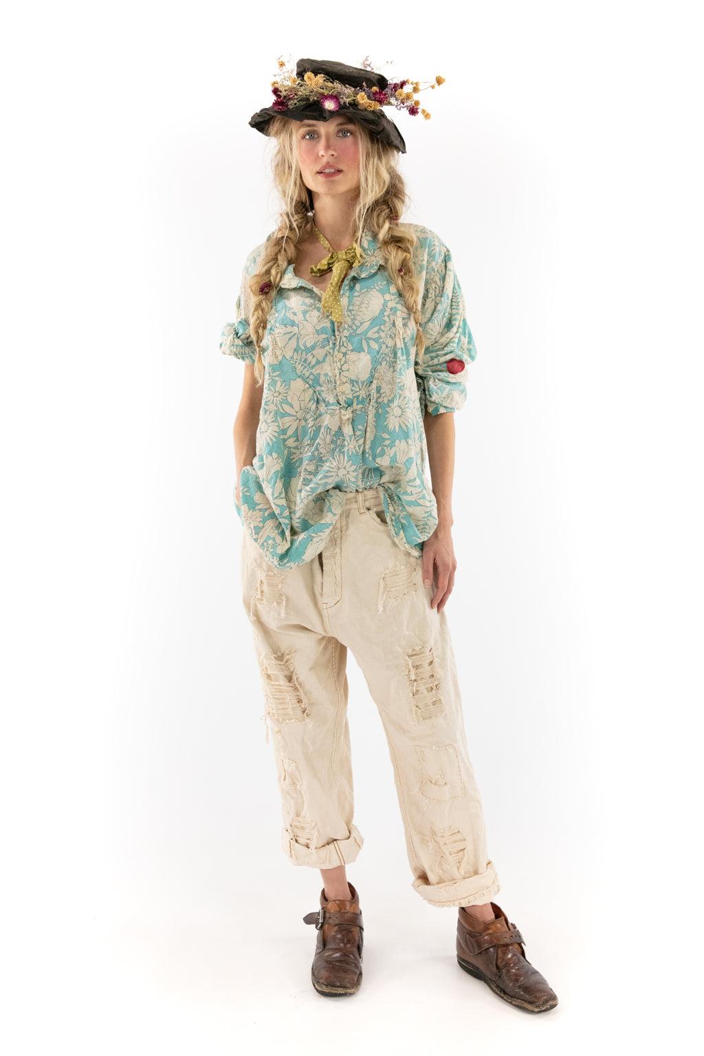 Woman in Magnolia Pearl artisan floral shirt, distressed pants, floral hat, whimsical vintage style
